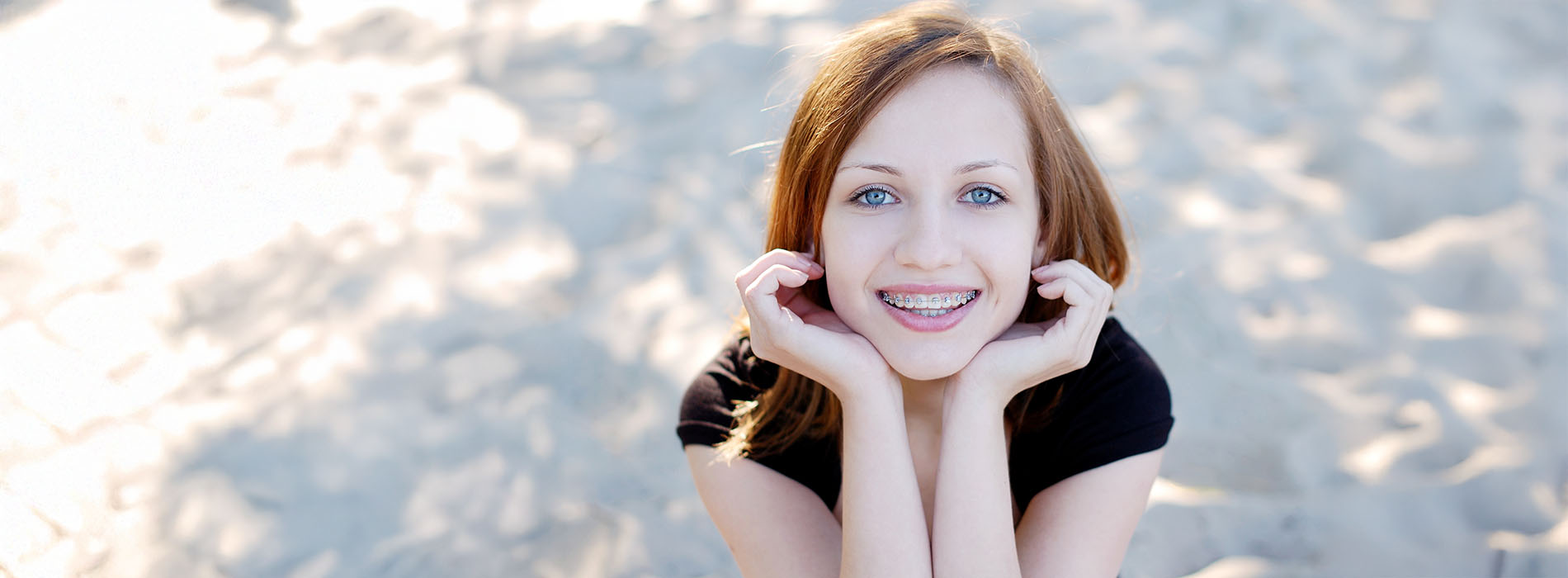 A woman with blonde hair is holding up a peace sign with her right hand while standing against a blue background.