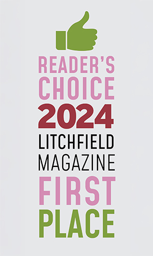The image features a graphic design with text overlaying a photograph. At the top, there s a stylized green checkmark with the word READER S CHOICE beneath it in bold, uppercase letters. Below this, a large number 2021 is prominently displayed, followed by the name LITCHFIELD MAGAZINE in smaller uppercase letters. A pink stripe separates the text from the photograph below. The photo shows a magazine cover with the headline FIRST PLACE and the subheadline READER S CHOICE 2021. The cover features a graphic element resembling a trophy or award, and there is a small pink ribbon with the text LITCHFIELD MAGAZINE on it. The overall style of the image suggests an advertisement or promotional material for a magazine that has won some sort of recognition in 2021. The design uses a clean, modern aesthetic with a color scheme that includes shades of green and pink.
