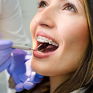 The image shows a person receiving dental care with an orthodontist, wearing braces, and having their teeth adjusted using a dental instrument, all in a clinical setting with a professional background.